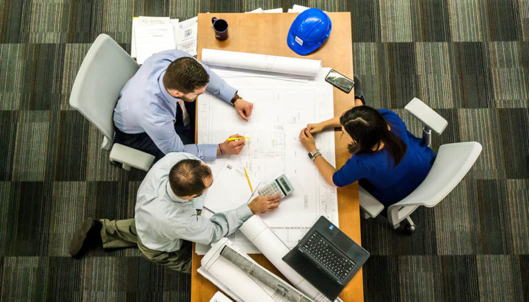 Overhead view of three people looking over a blueprint