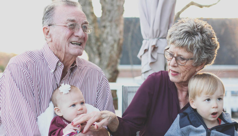 Two elderly people holding a baby and a toddler